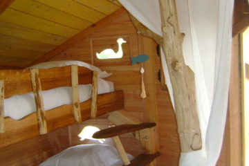 r-la-jumelle-1- Cabane perchée avec un lit en bois et une fenêtre en forme doiseau.