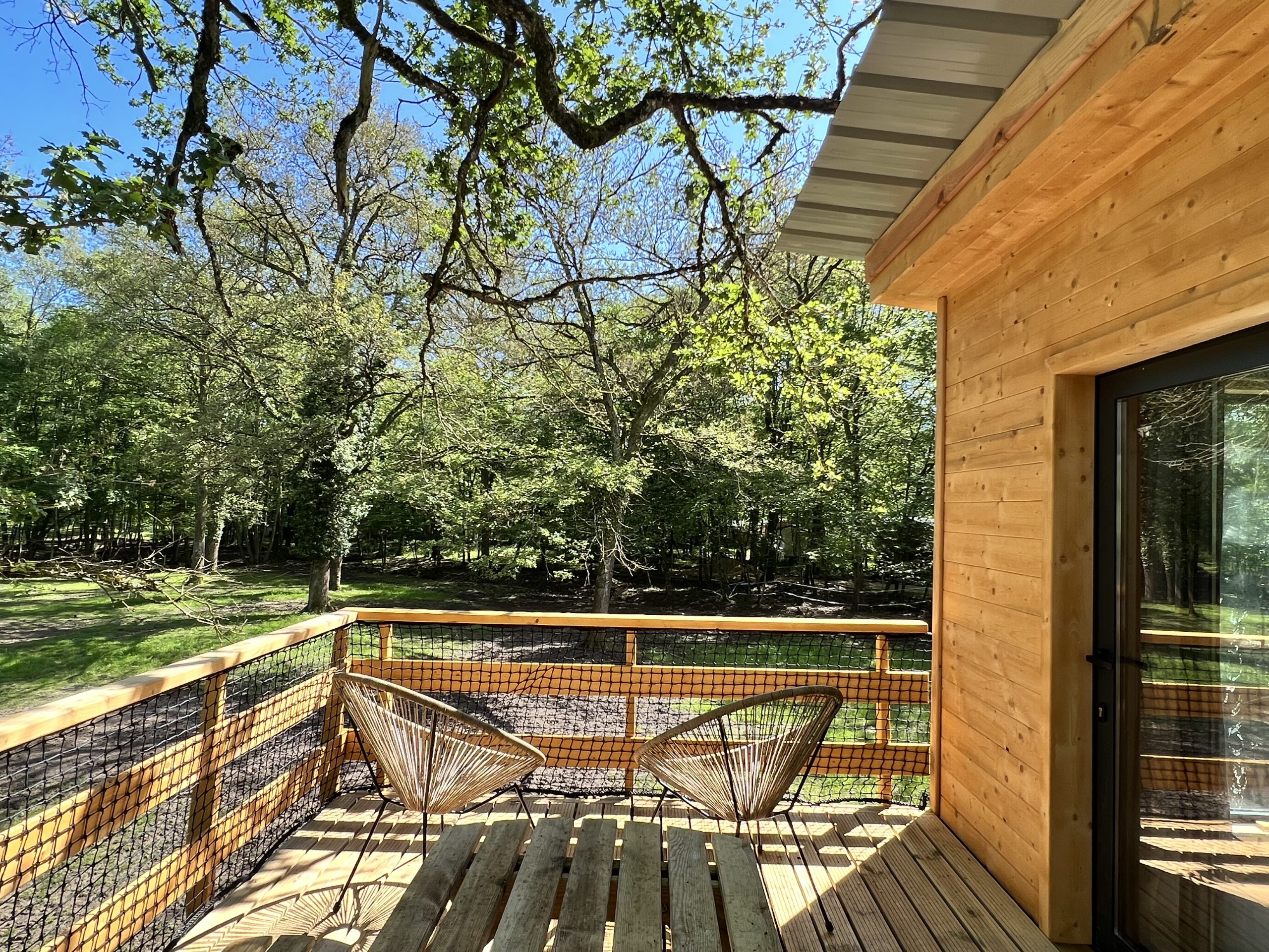 Cabane Clairière domaine de la dombes (5) Cabane en bois avec terrasse, entourée de verdure en Auvergne-Rhône-Alpes.