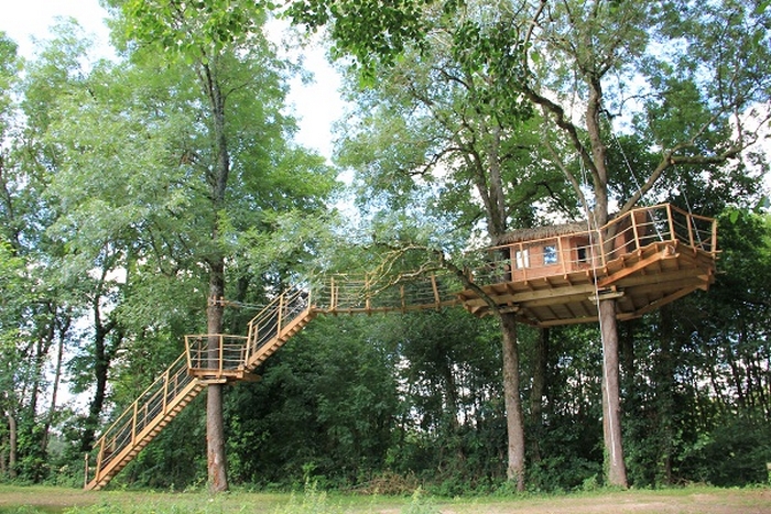 Feuilles (2) Cabane perchée dans les arbres, entourée de verdure, offrant une vue panoramique.