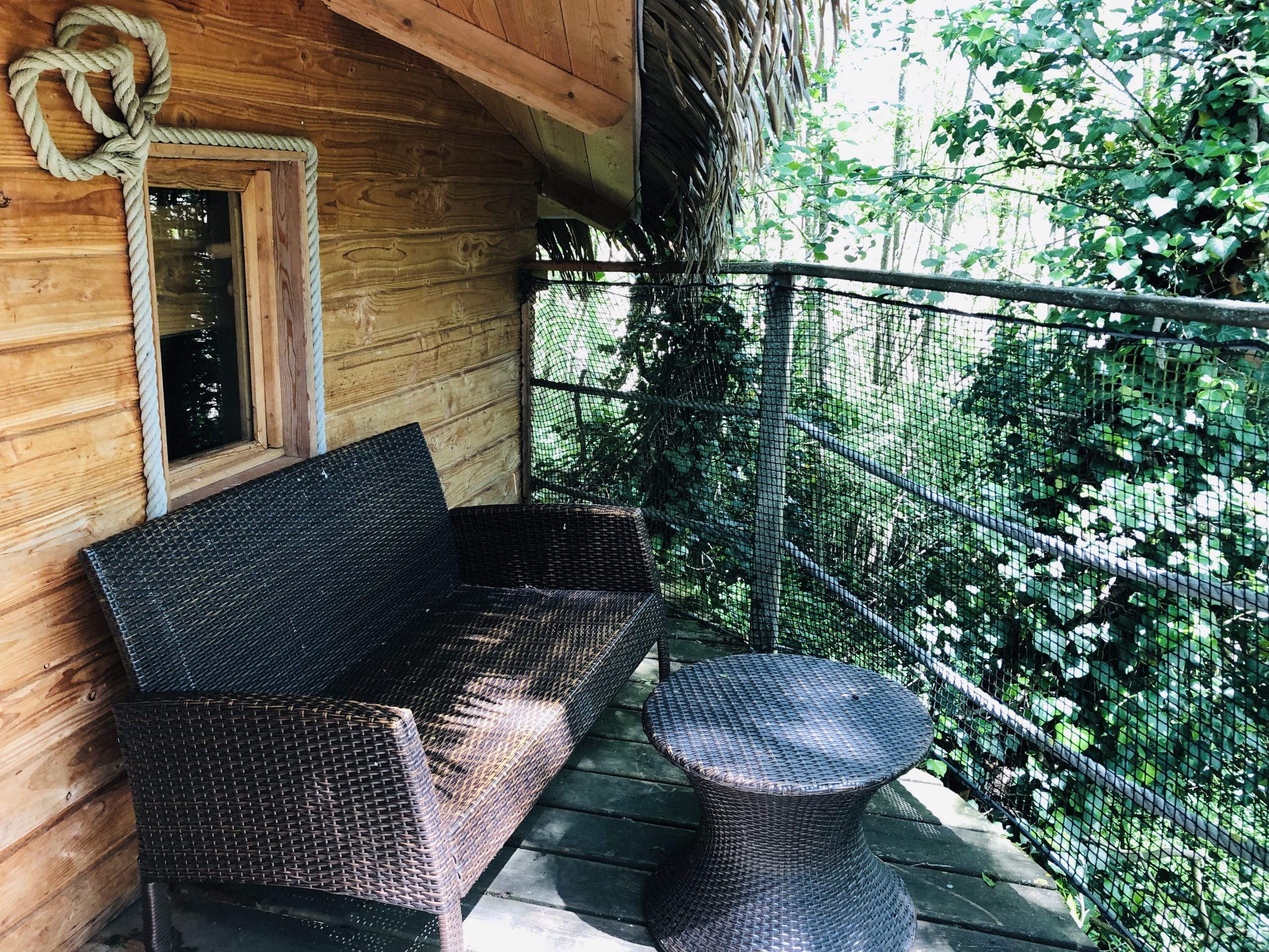 Feuilles (3) Cabane perchée en Auvergne-Rhône-Alpes avec terrasse en bois et mobilier en rotin.