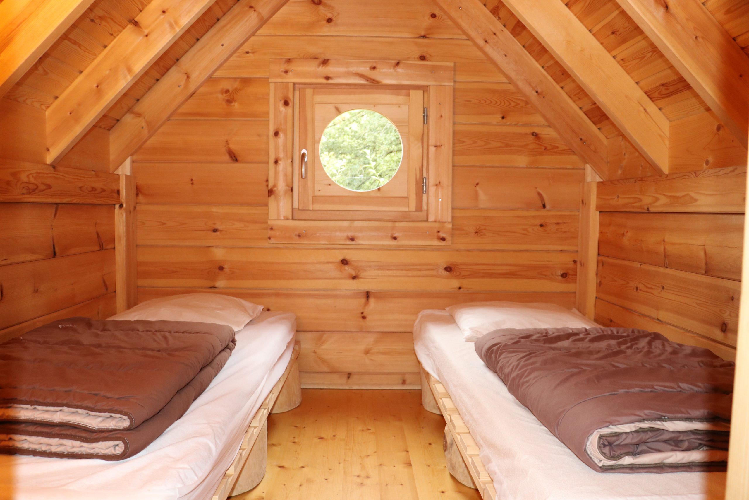 IMG_5327 Chalet en bois avec deux lits simples et une fenêtre ronde, ambiance chaleureuse.