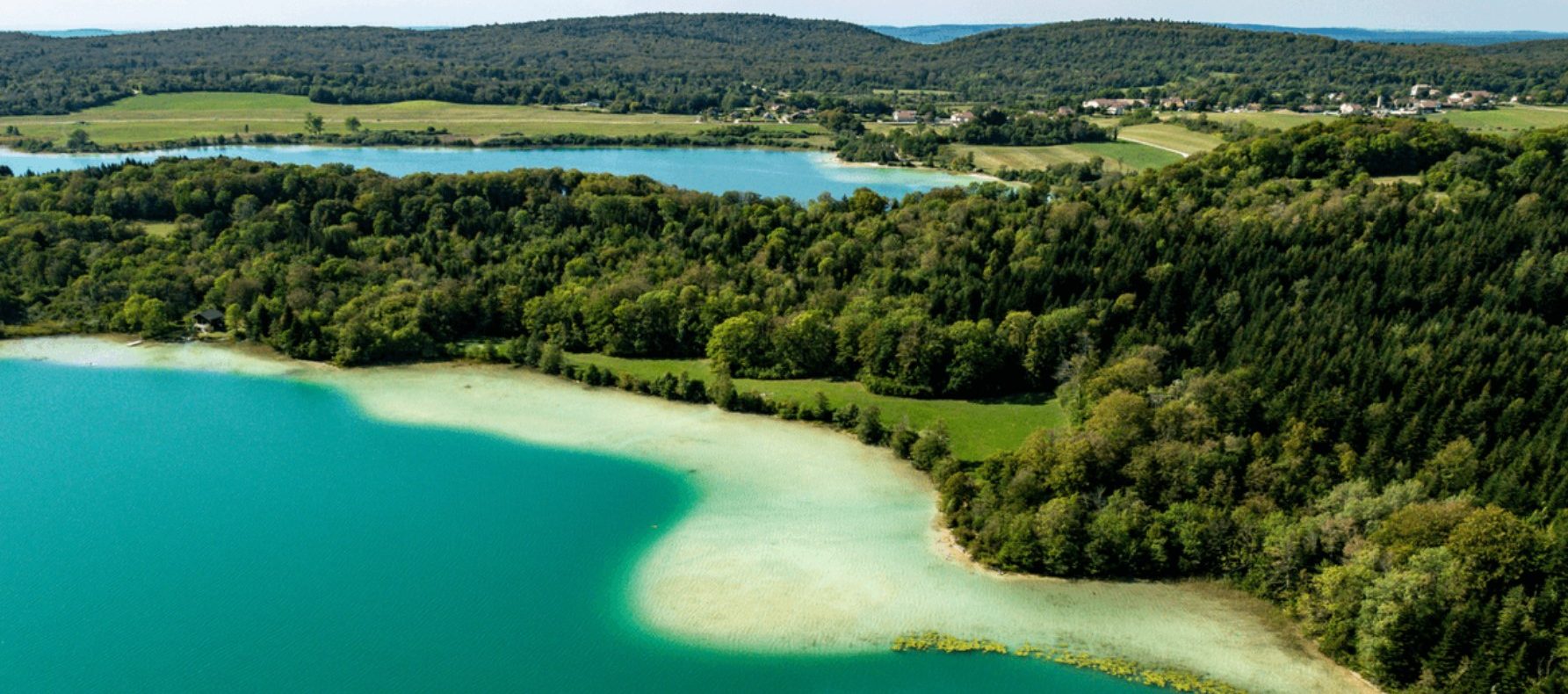 Hébergement en pleine nature avec vue panoramique sur un lac turquoise et des collines verdoyantes.