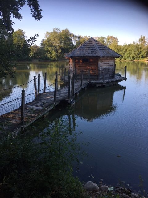 LORNAGE Marie (3) Cabane sur pilotis au bord dun lac, entourée de verdure en Auvergne-Rhône-Alpes.