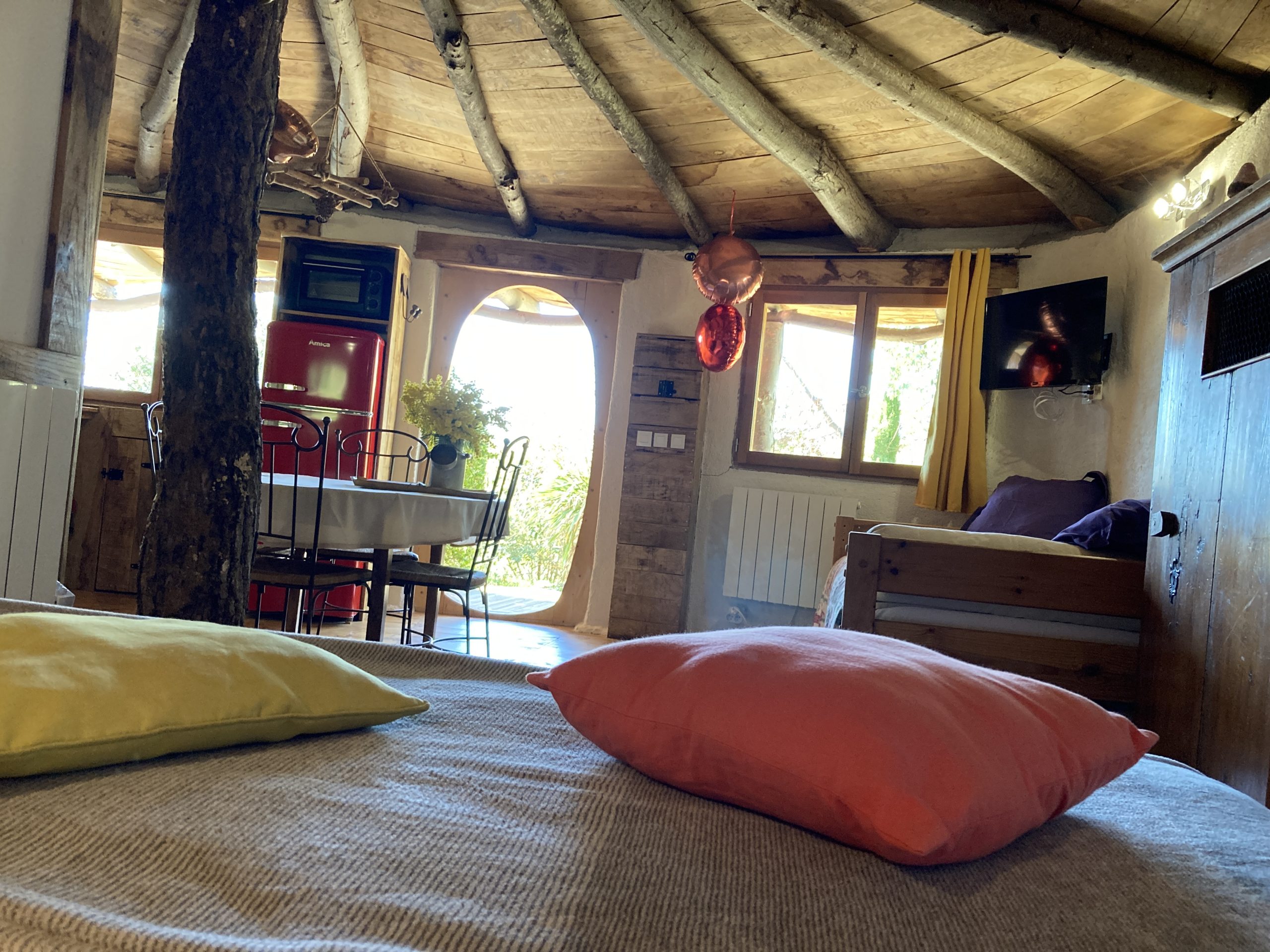 IMG_3058 Hébergement insolite en cabane, intérieur chaleureux avec poutres en bois et coussins colorés.