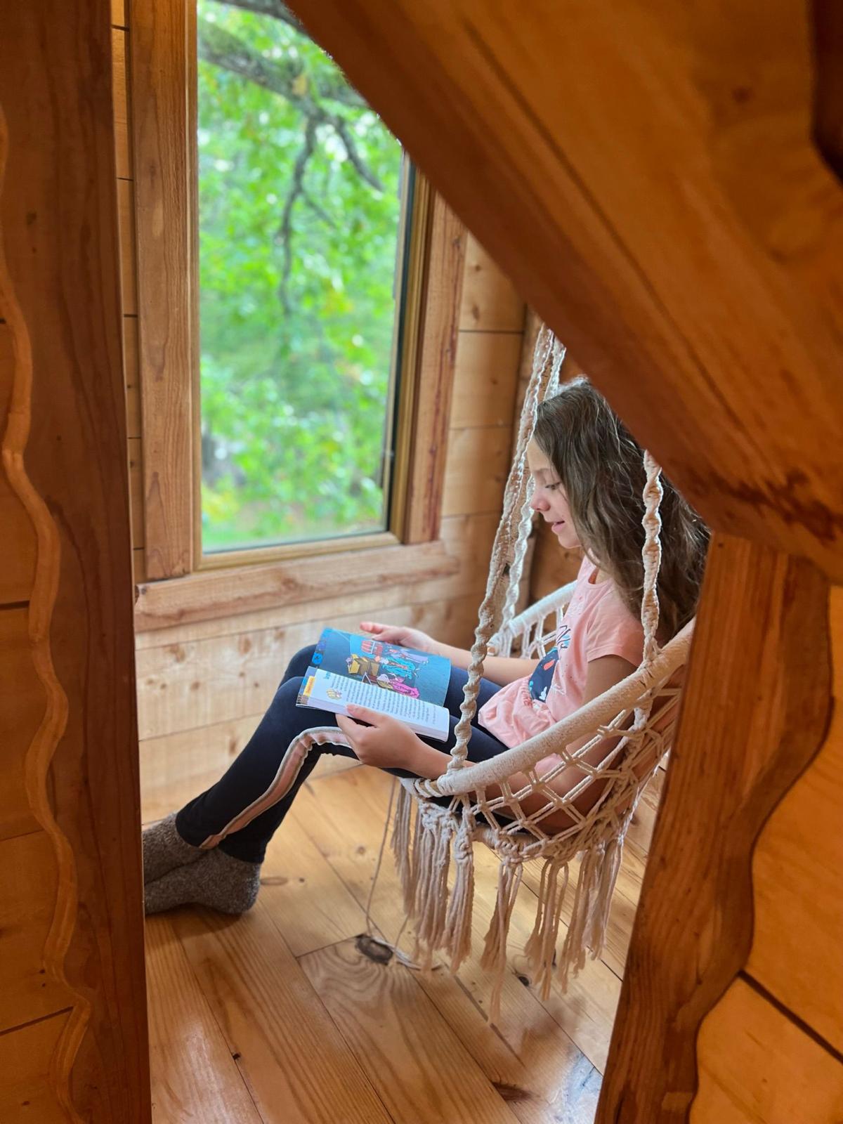 WhatsApp Image 2024-09-04 at 16.18.15 Cabane perchée en Auvergne-Rhône-Alpes, enfant lisant dans un hamac suspendu.