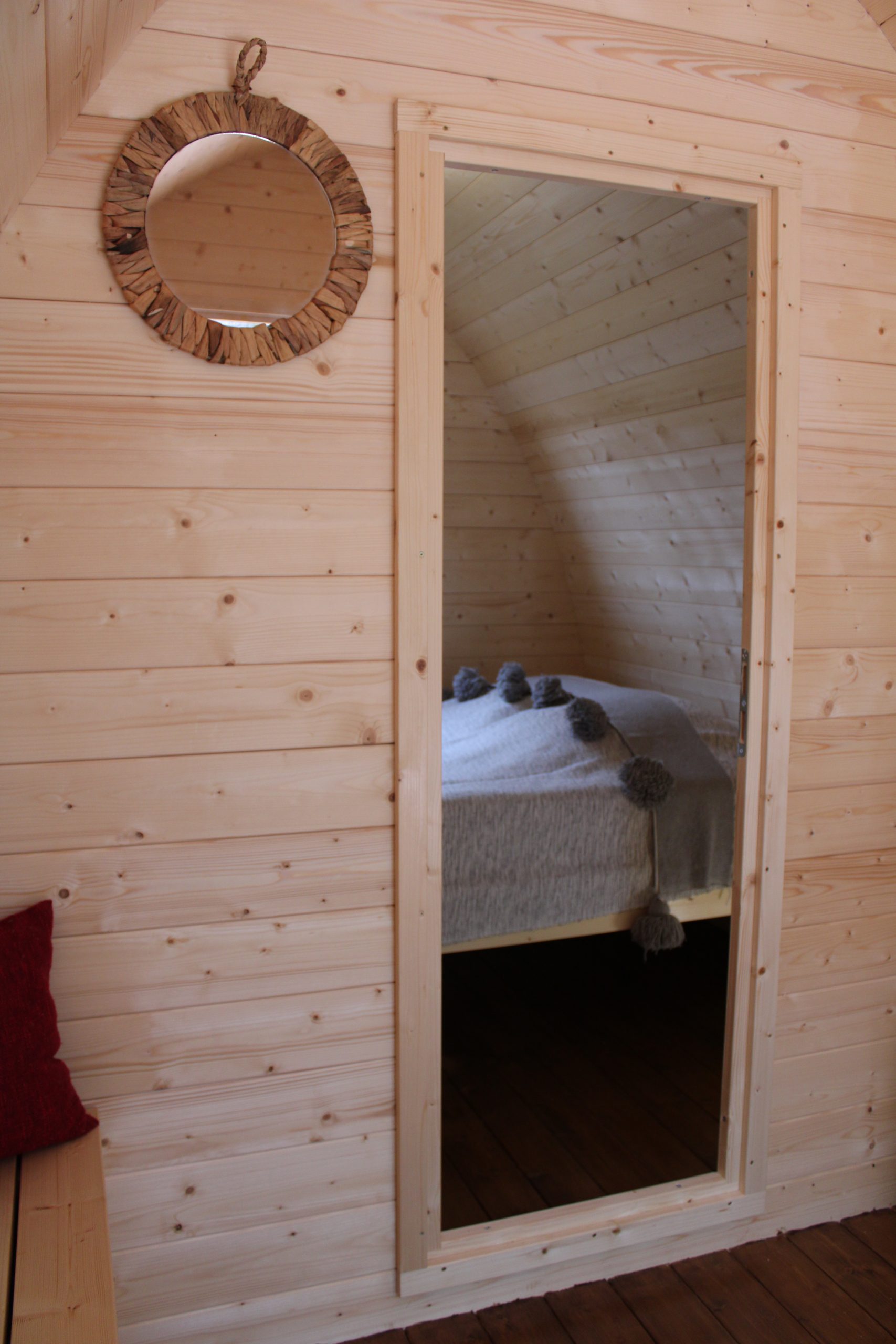 IMG_8399 Intérieur dun hébergement insolite en bois, lit cosy et miroir rond en rotin.