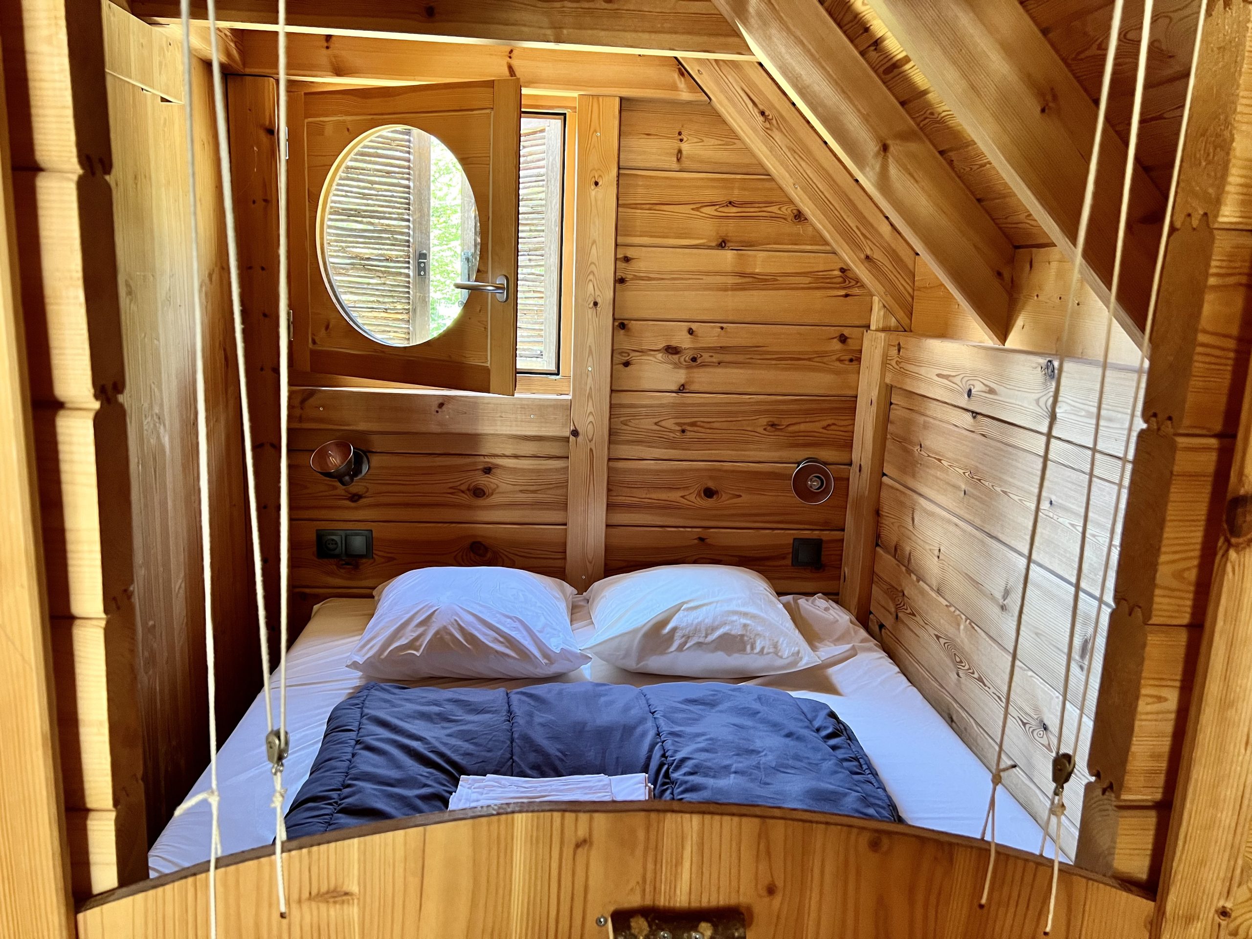 Sanglier lit rdc Cabane en bois cosy avec lit douillet et fenêtre ronde, située en Auvergne-Rhône-Alpes.