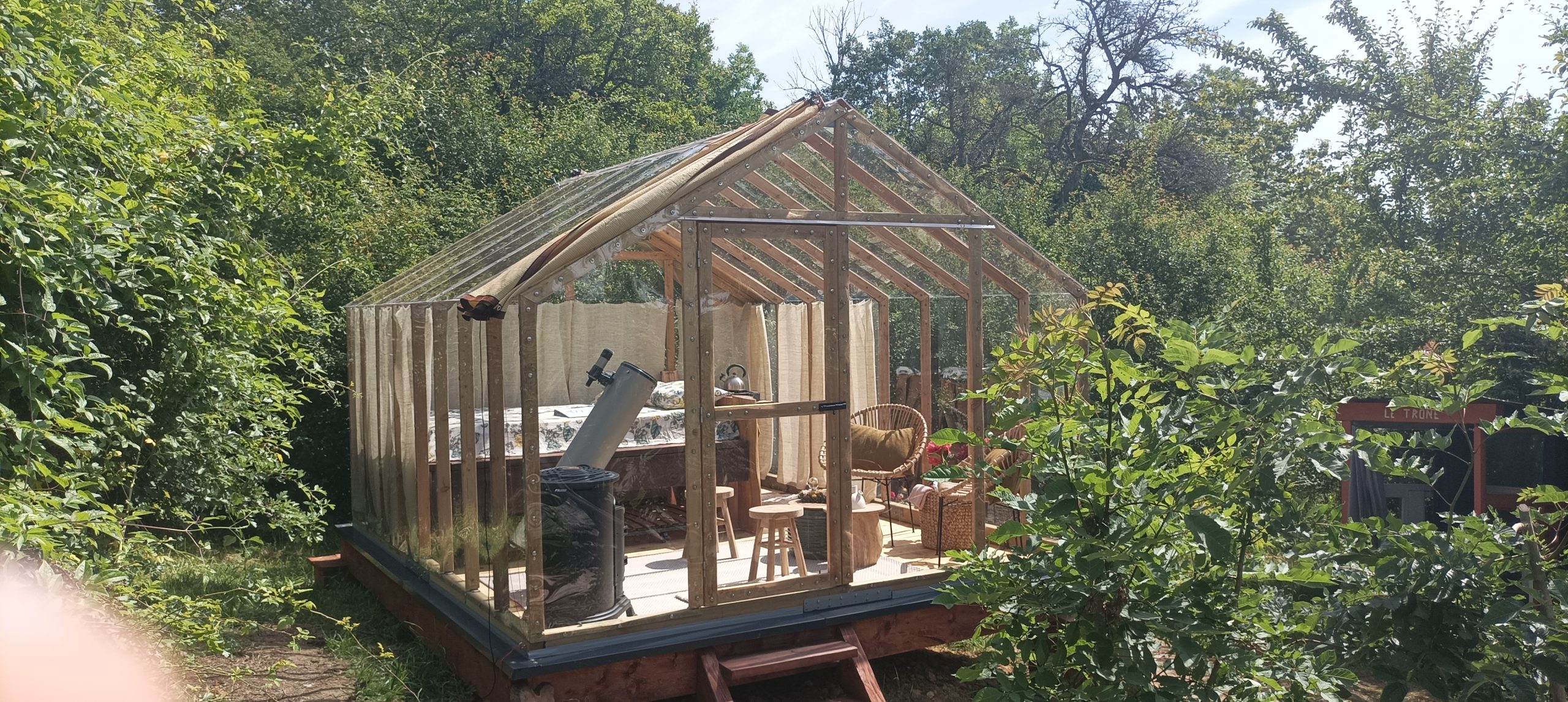 cabane du rêveur - estivale (3) Hébergement insolite : serre en bois avec mobilier cosy, entourée de verdure.
