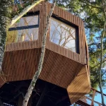 Cabane dans les arbres en bois, avec de grandes fenêtres et vue sur la nature environnante.