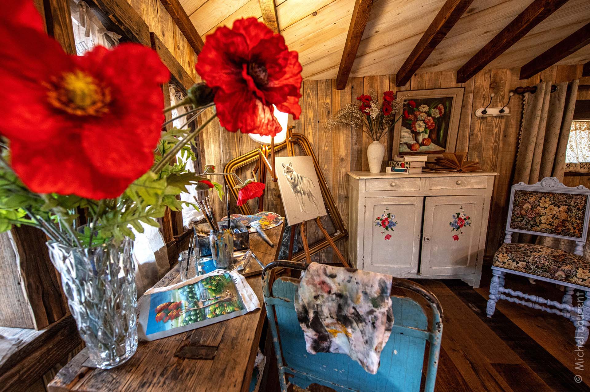 artistes-atelier-insolite-location Cabane artistique en Grand-Est, décorée de fleurs rouges et dœuvres dart.