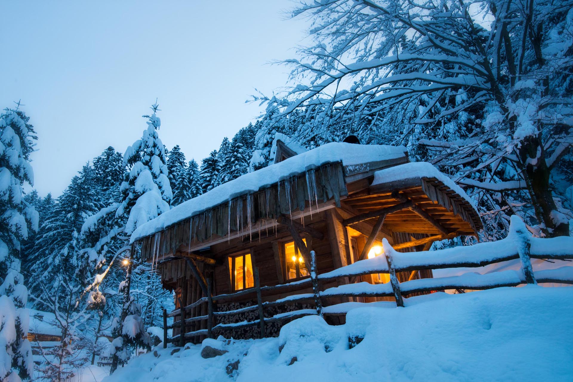 cabane-dans-les-arbres-la-bresse-hiver-paysage-neige Cabane en bois dans la neige, illuminée par une douce lumière chaleureuse.
