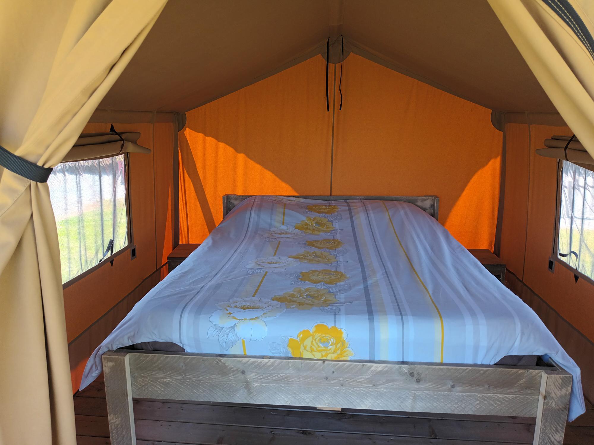 20230602_134355 Tente safari confortable avec un lit douillet et des murs orange lumineux.