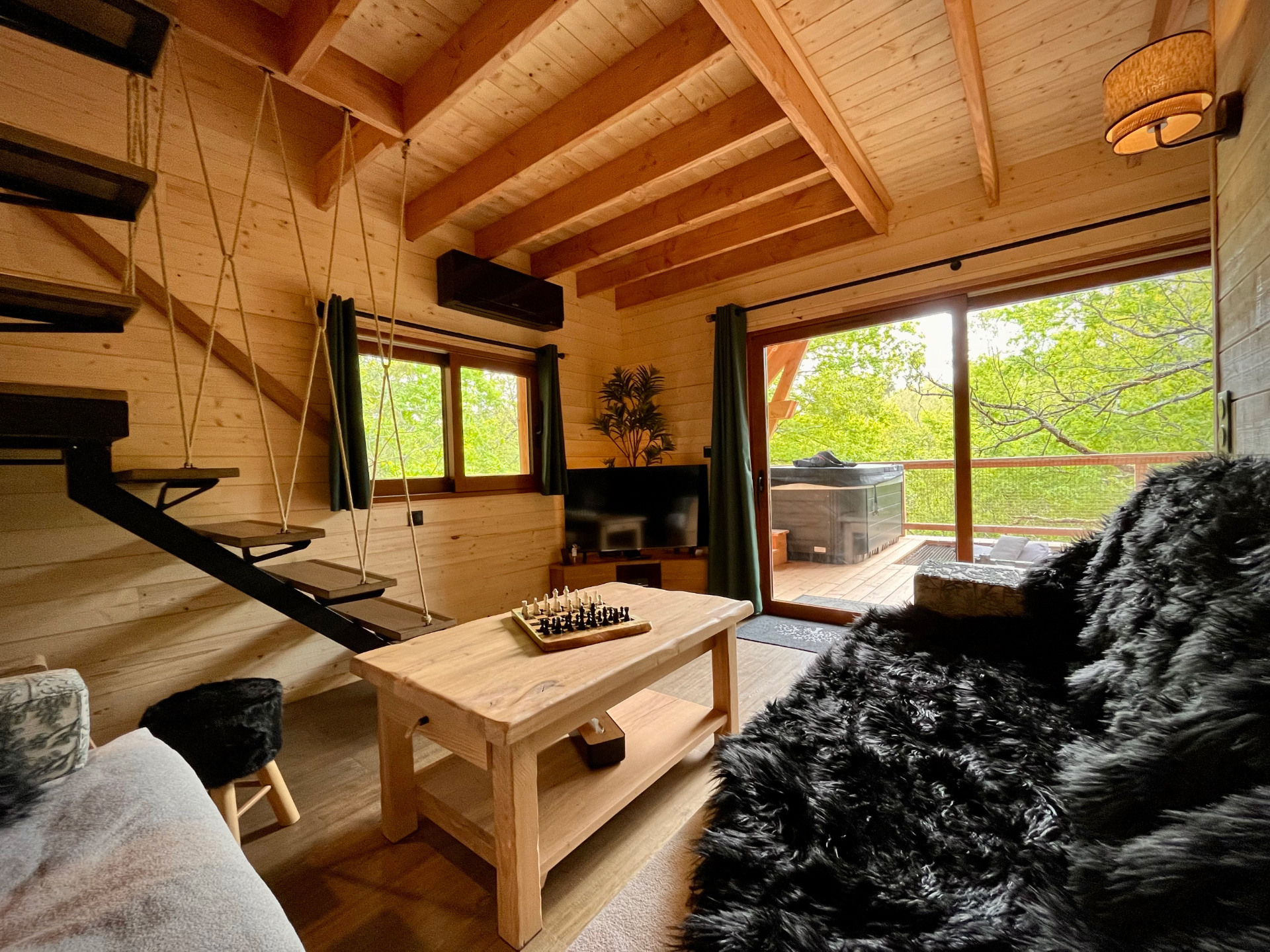 Chalet style dans les arbres cocooning plaid Cabane en bois avec intérieur chaleureux, vue sur la nature et jacuzzi extérieur.