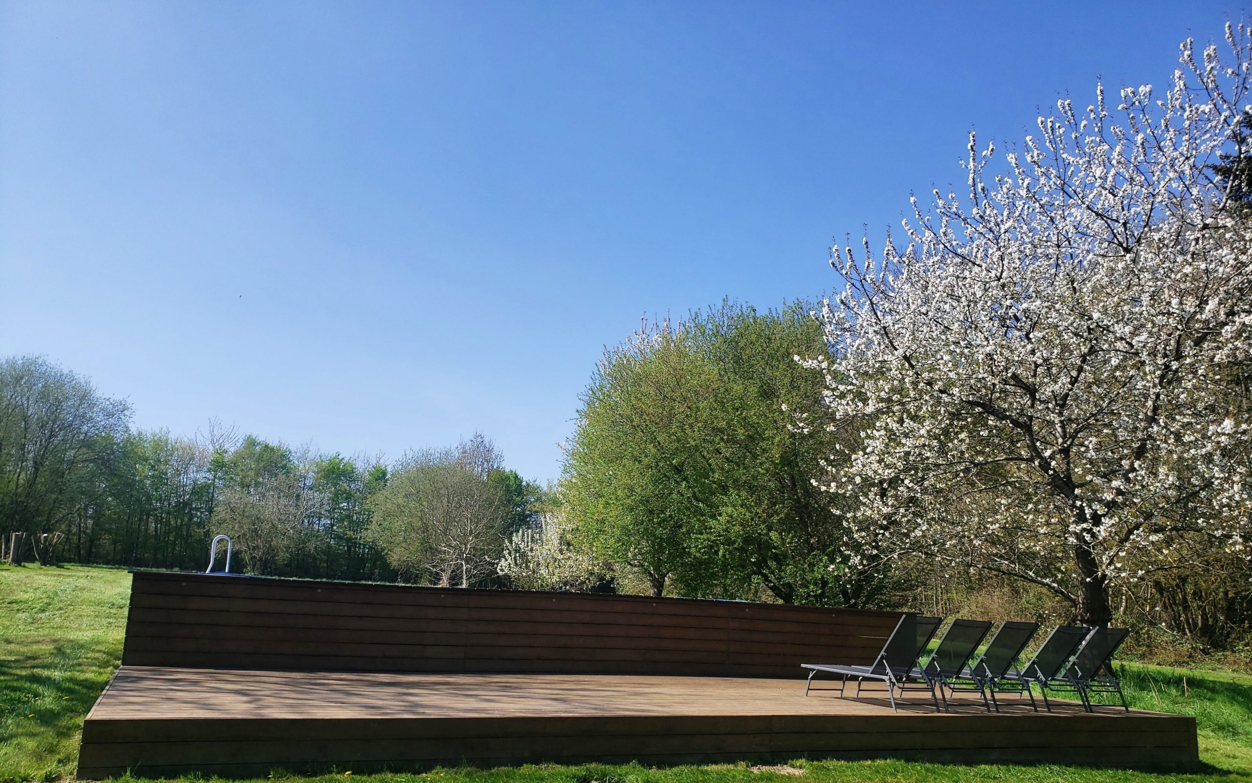 20250410_121822 Hébergement insolite en Haute-Normandie avec terrasse en bois et arbres en fleurs.