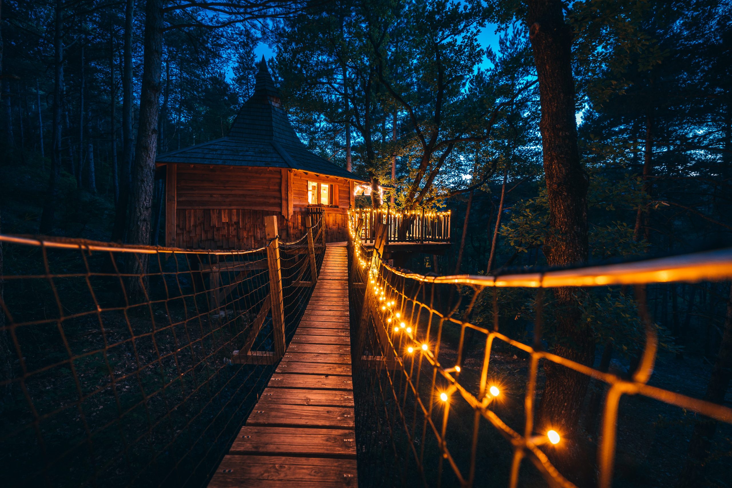 Copie de 04072022-5X2A1603 Cabane perchée en bois, illuminée par des guirlandes, au cœur des arbres.