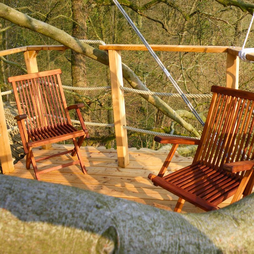 Grand hêtre2 Cabane dans les arbres avec une terrasse en bois et deux chaises confortables.