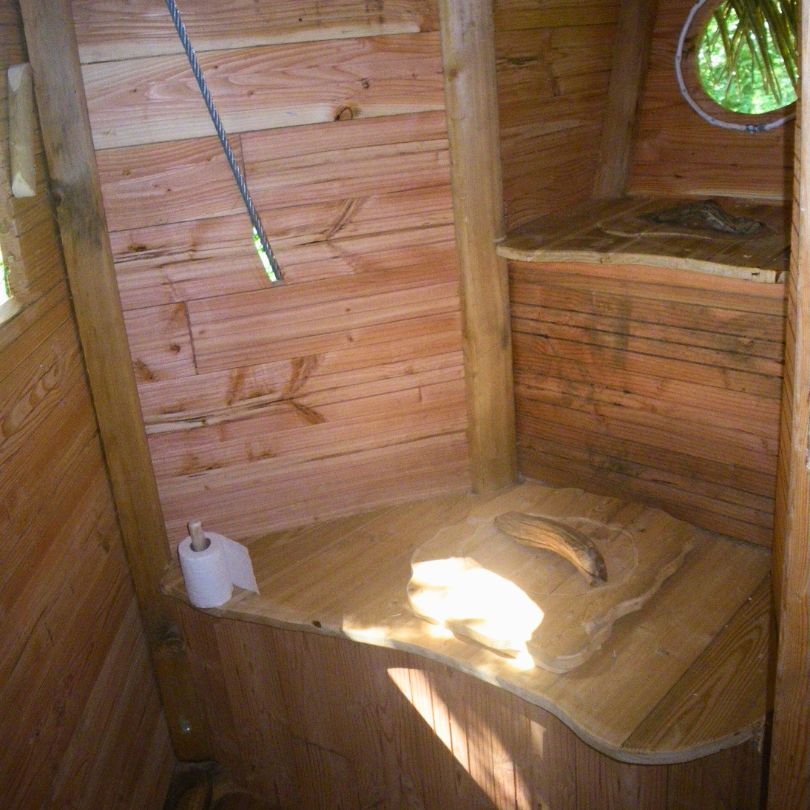 La baron perché3 Cabane en bois avec un intérieur chaleureux, banc en bois et fenêtre ronde. Ambiance cocooning.
