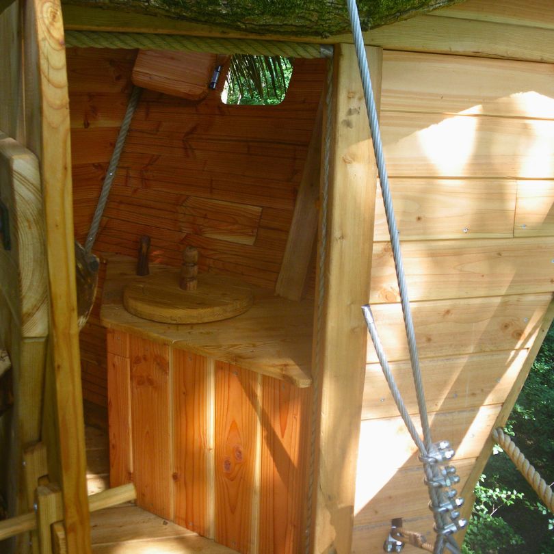 terriers4 Intérieur d'une cabane dans les arbres, avec des murs en bois et un coin toilette rustique.