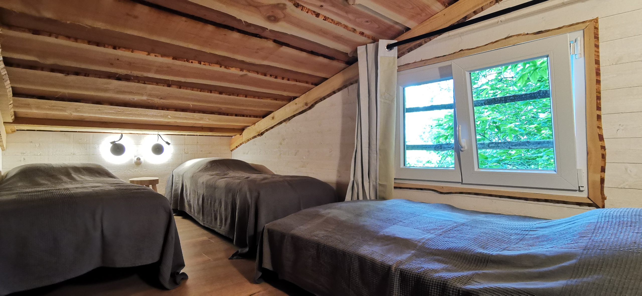 12 Chalet cosy avec lits simples, poutres apparentes et vue sur la nature à travers la fenêtre.