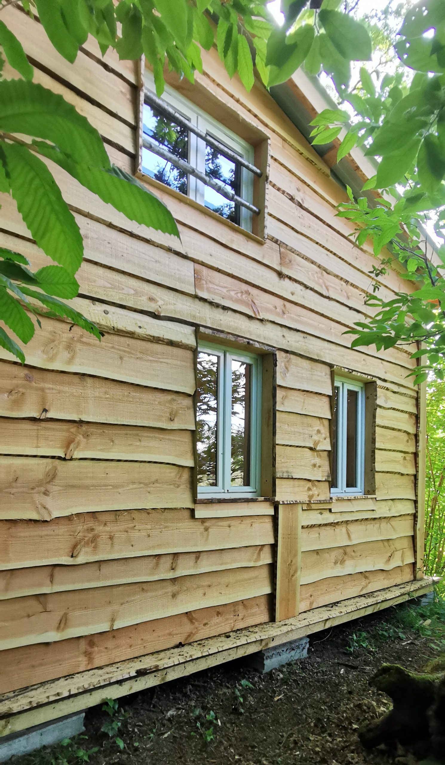 14 Cabane en bois au milieu de la verdure, avec des fenêtres encadrées de bois naturel.