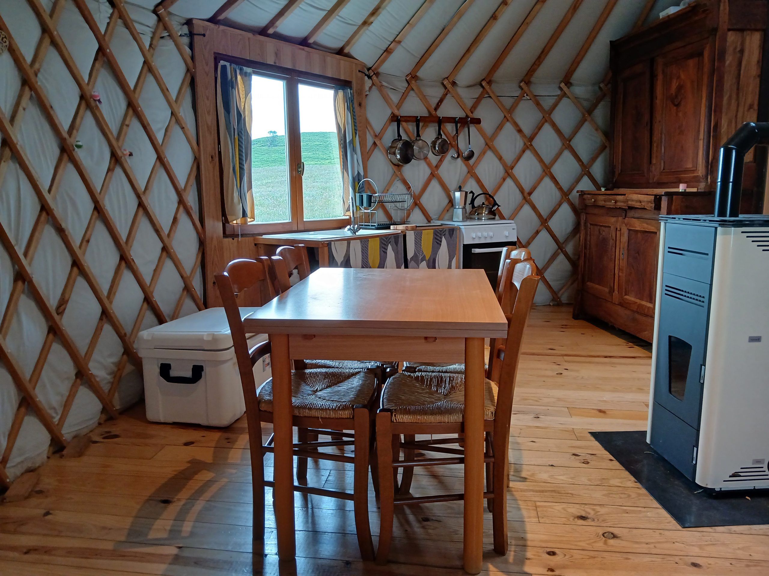 20240625_181529 Intérieur d'une yourte chaleureuse, avec table en bois, chaises et cuisine équipée.