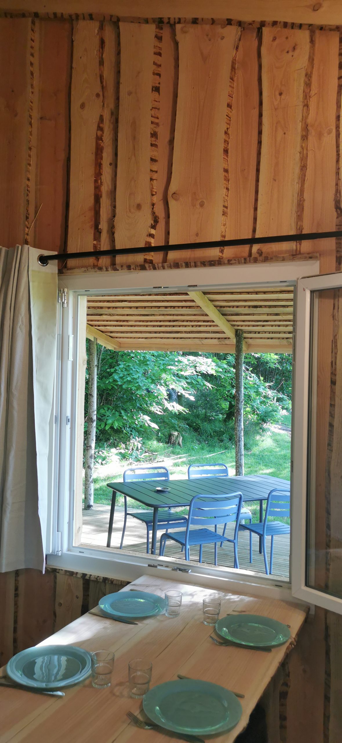 4 Vue sur une terrasse en bois depuis un chalet en bois, avec des chaises bleues et verdure