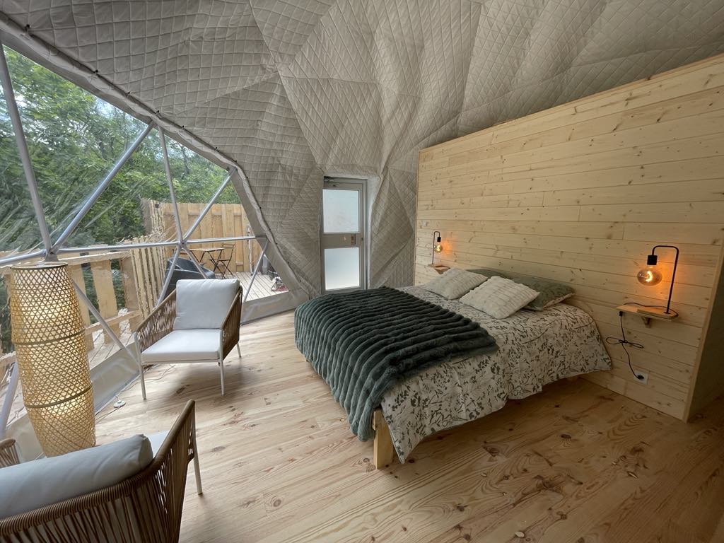 893452d0-f3c4-4f8a-bbcd-662daa85fe75 Dôme géodésique avec intérieur en bois, lit douillet et vue sur la nature.