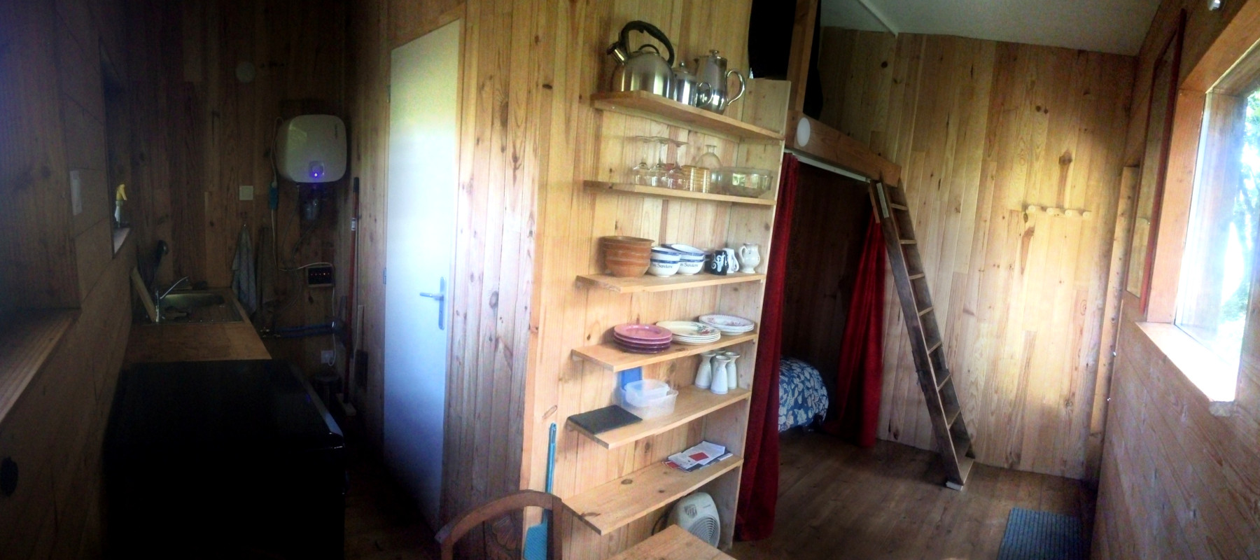 Cabane01 Cabane en bois chaleureuse avec étagères en bois, kitchenette et échelle menant à une chambre.