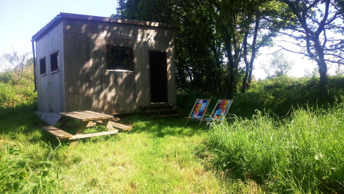 Cabane02 Cabane en bois entourée de verdure, avec une terrasse en bois et des tableaux colorés à l'extérieur.