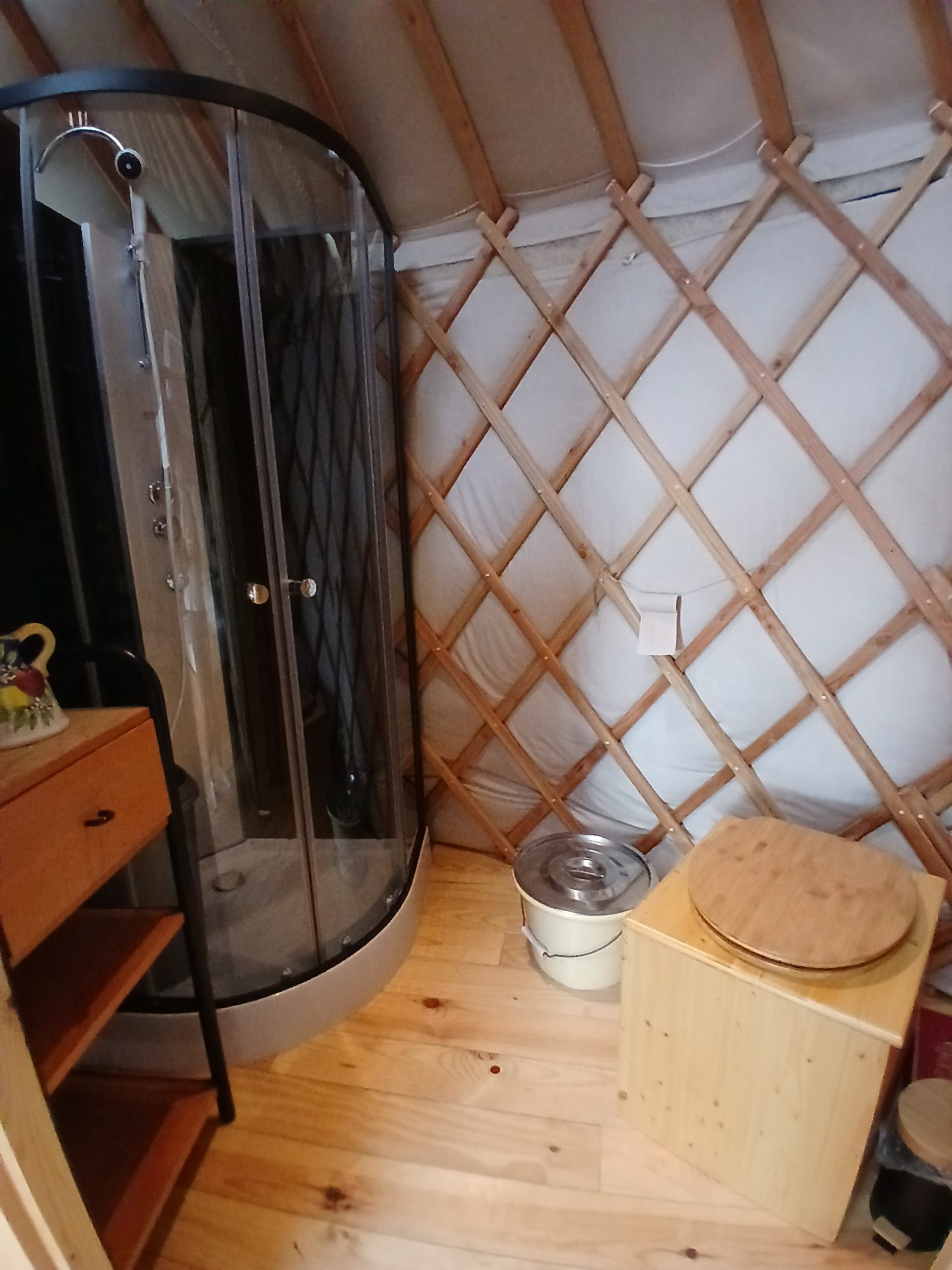 Coin toilette Intérieur d'une yourte avec douche moderne, bois clair et murs en toile. Ambiance cosy et originale.