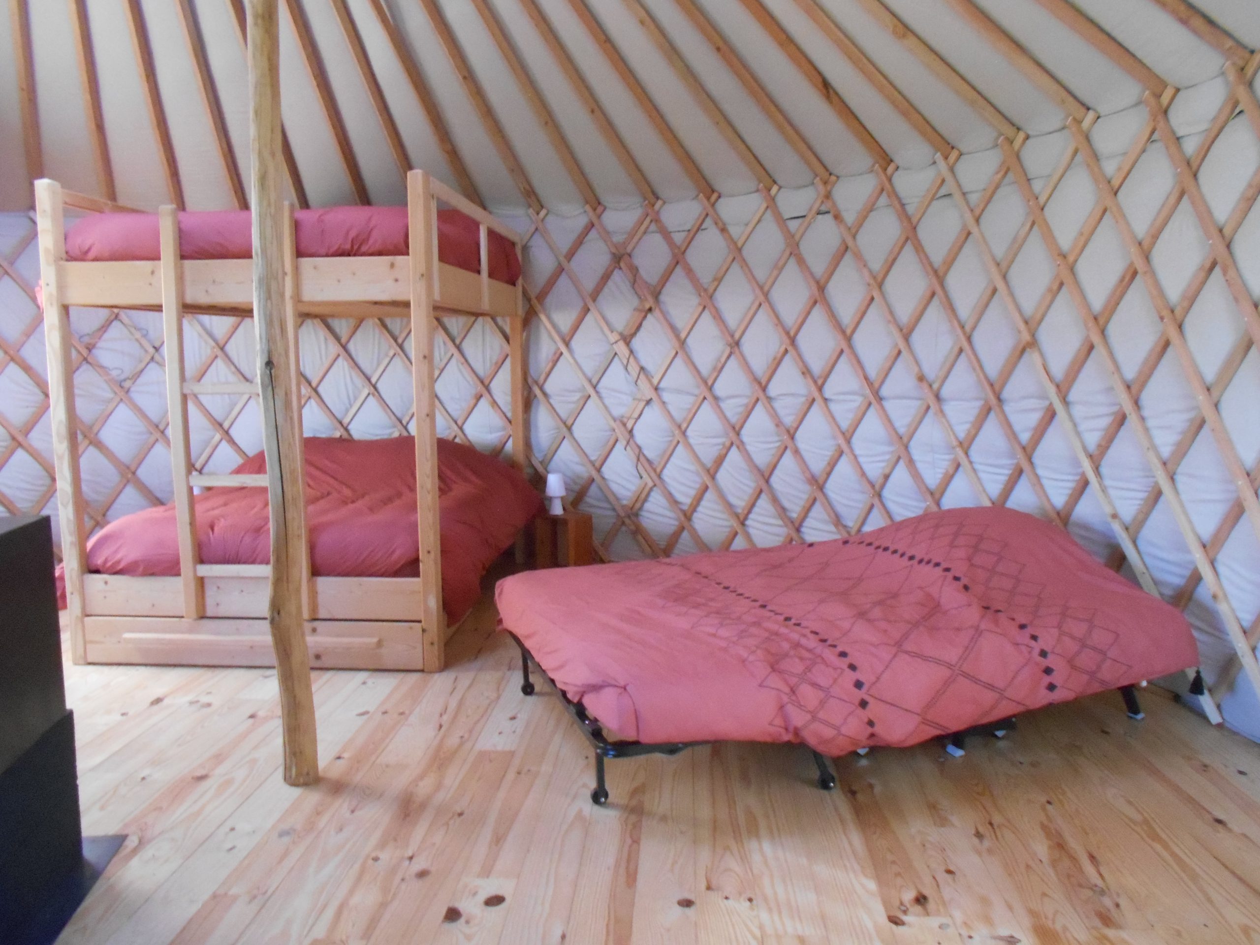 Côté chambre Intérieur d'une yourte avec lits superposés et un lit double, ambiance chaleureuse en bois.