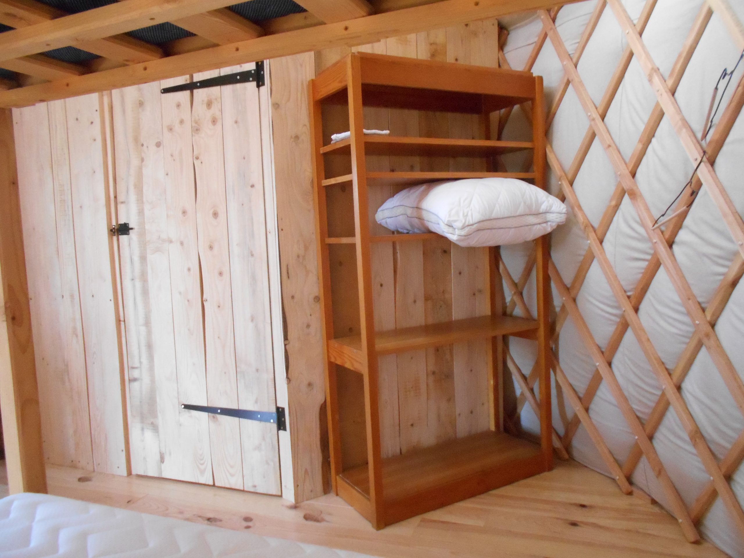 Etagère pour ranger vos sacs, vétements... Intérieur d'une yourte en bois, avec étagère et lit, ambiance chaleureuse et naturelle.