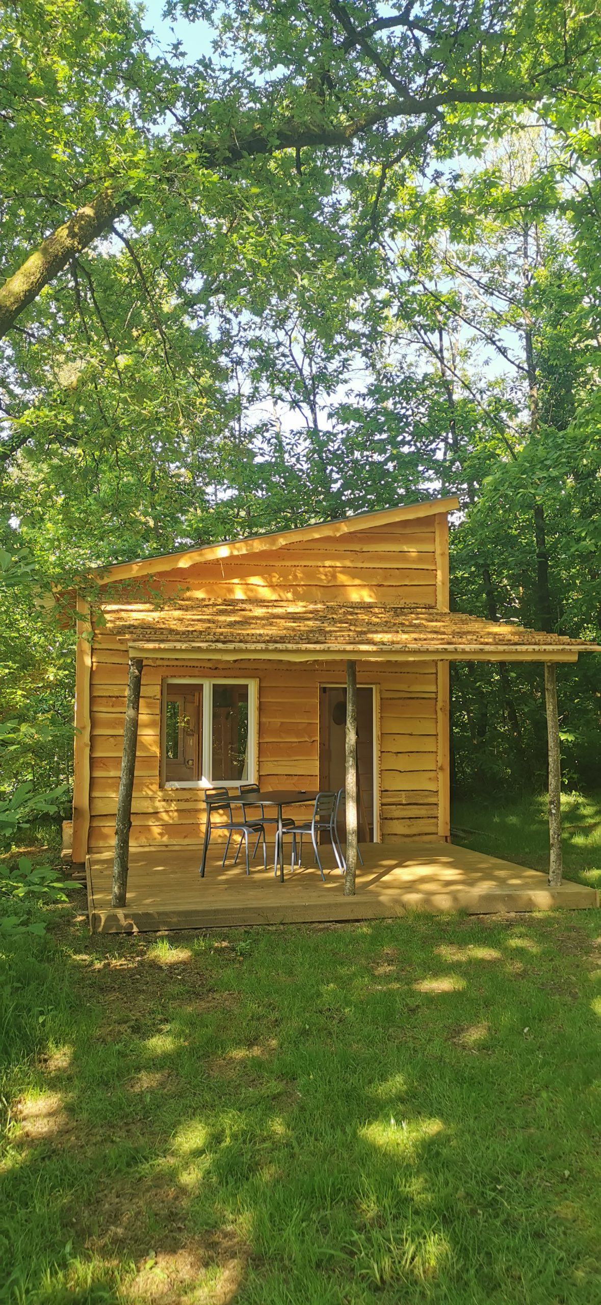IMG_20250514_175909 Charmante cabane en bois, entourée d'arbres, avec une terrasse et des chaises.