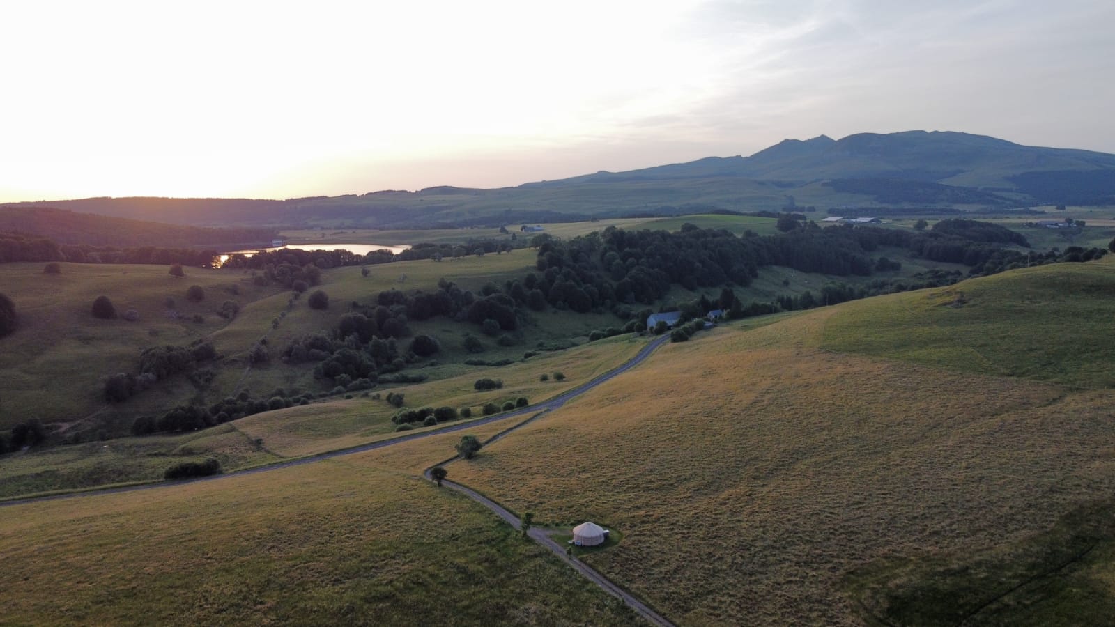 WhatsApp Image 2025-06-30 at 17.35.02 Yourte isolée au cœur d'un paysage verdoyant, avec des collines et un lac en arrière-plan.