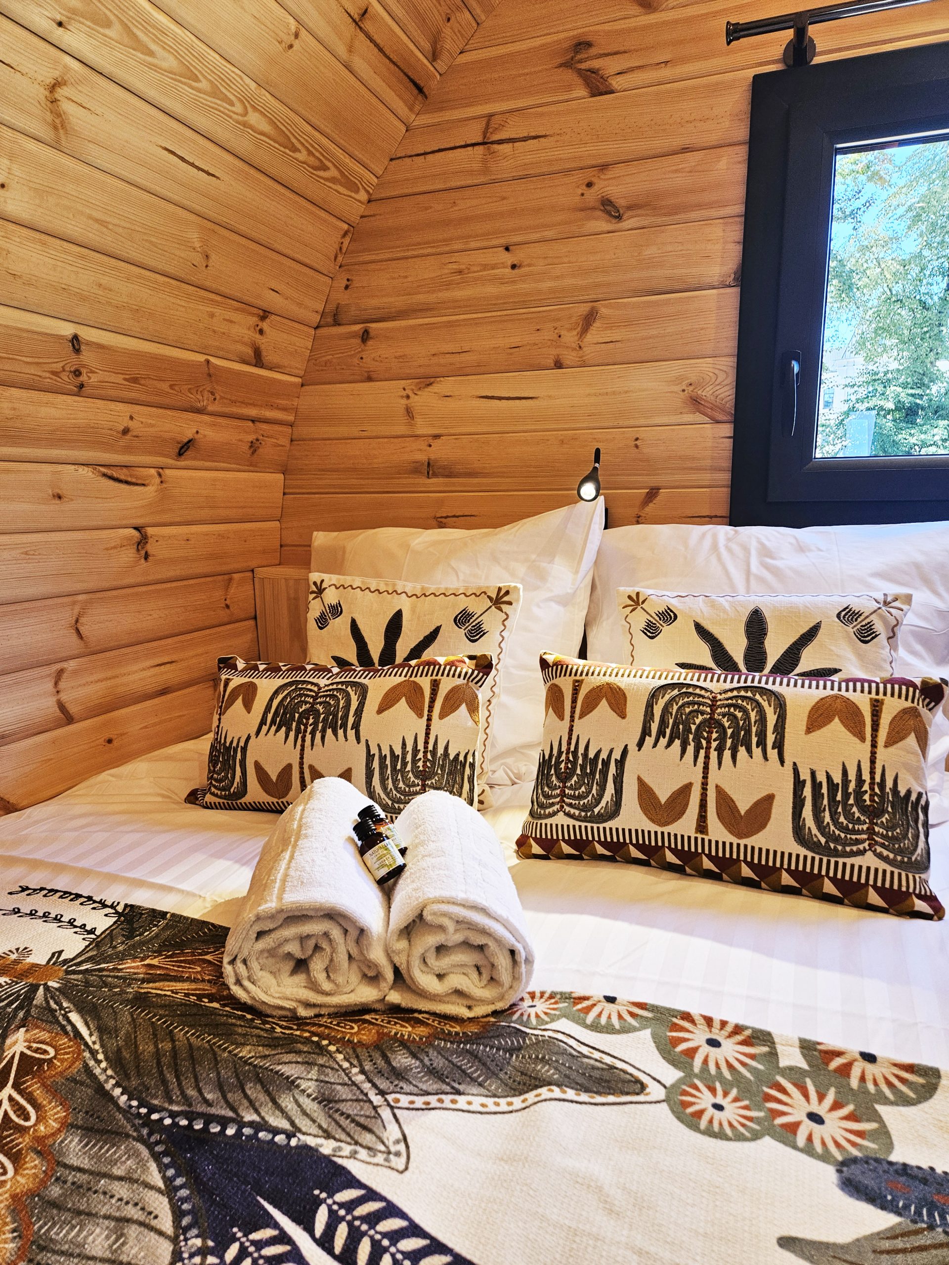 chambre_zoom_palmeraie Cabane en bois chaleureuse avec literie élégante et coussins décoratifs. Ambiance cocooning.