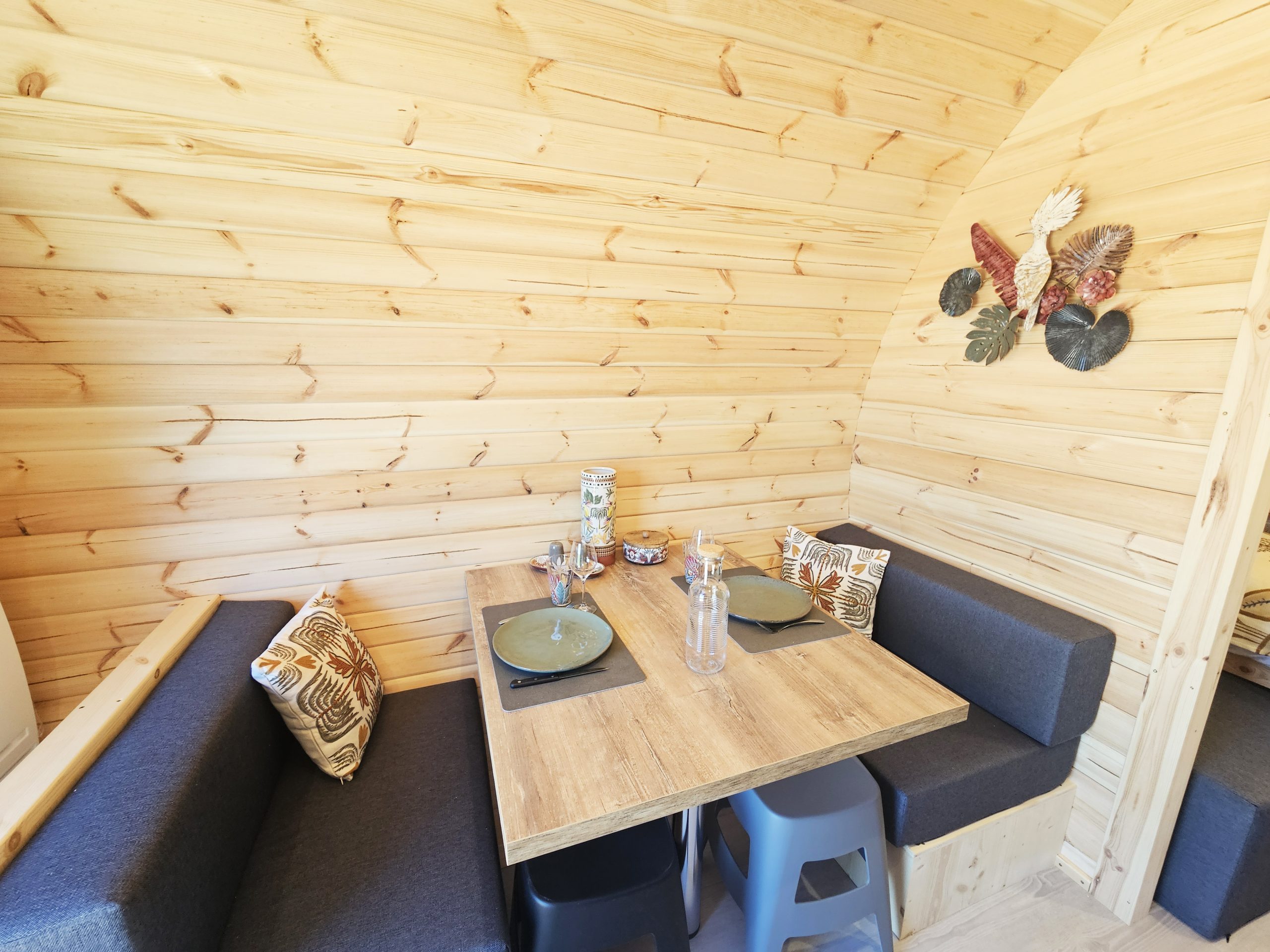 coin_repas_2_palmeraie Intérieur chaleureux d'un chalet en bois, avec table en bois et banquettes confortables.