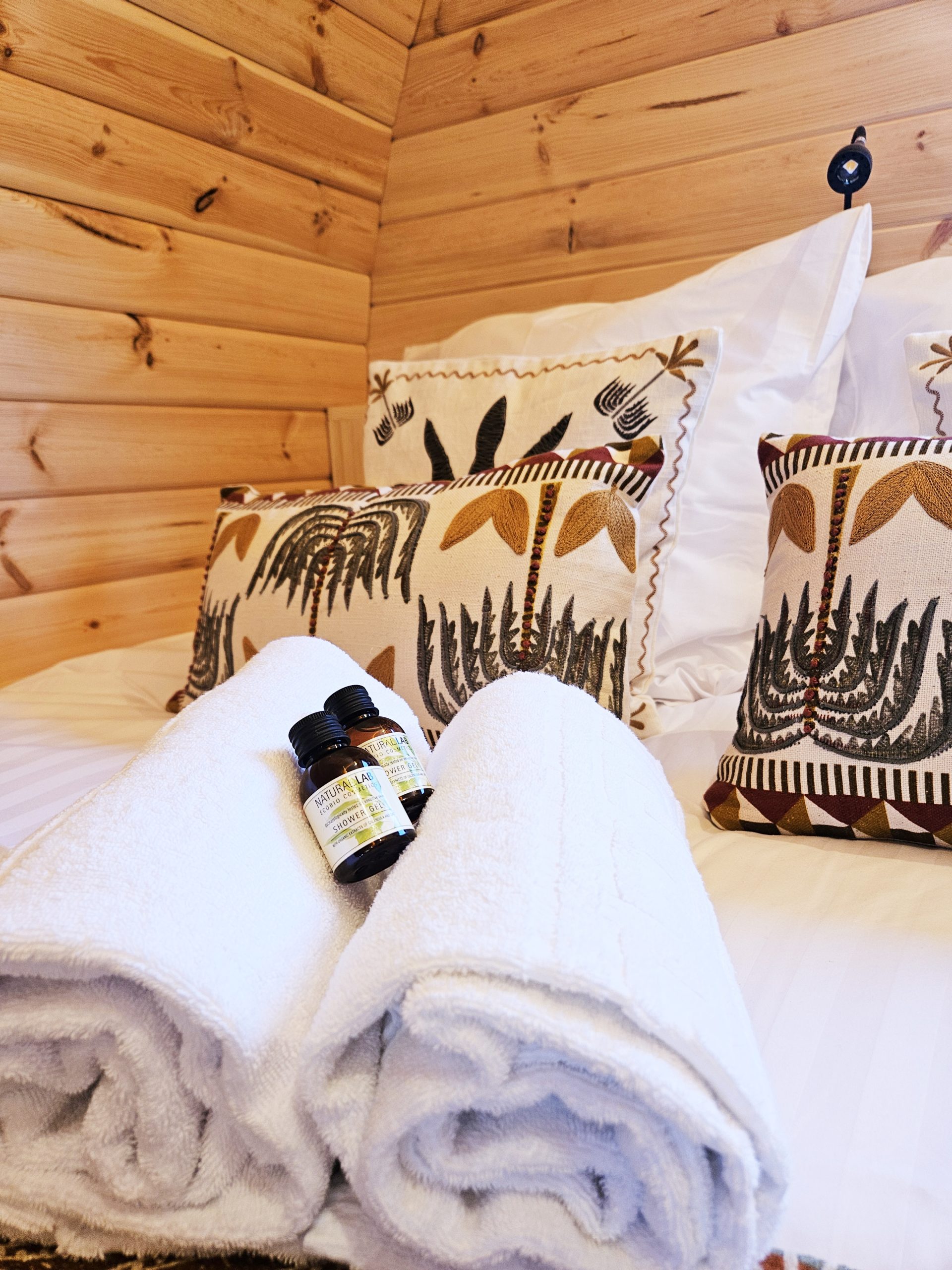 lit_palmeraie Chalet en bois chaleureux avec literie douillette et serviettes blanches, ambiance nature.