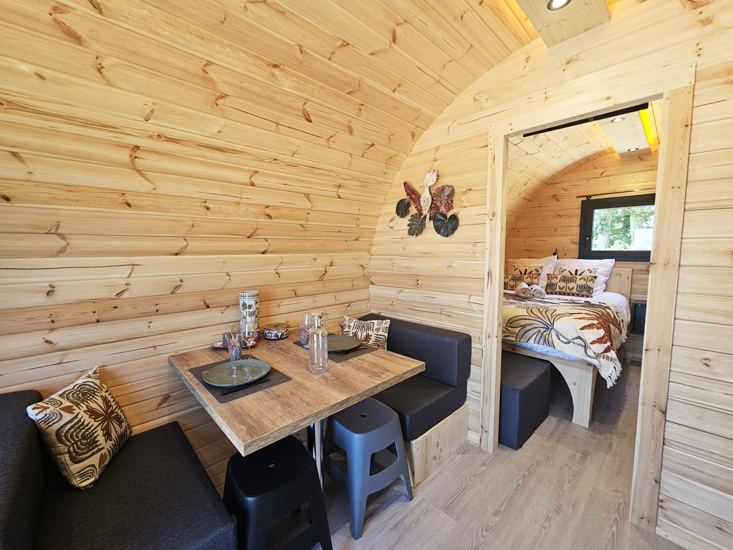 vue_ensemble_repas_couchage_palmeraie Intérieur chaleureux d'un hébergement insolite en bois, avec coin repas et lit douillet.
