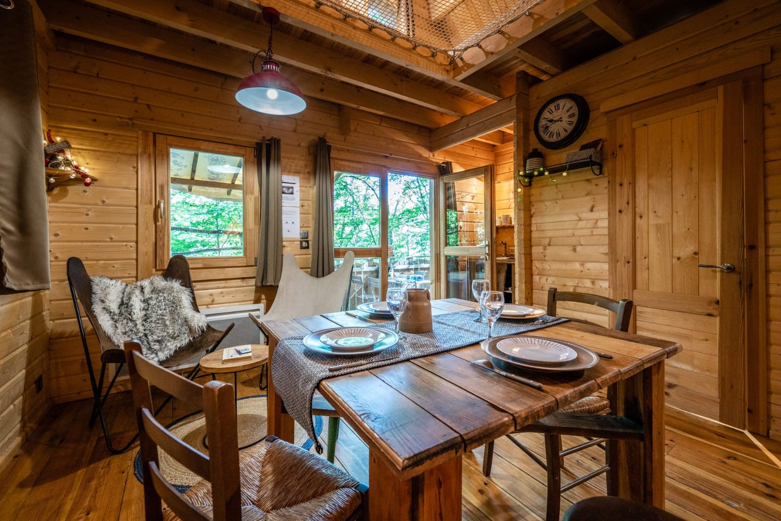 IMG-20250707-WA0015 Cabane en bois chaleureuse avec table en bois, chaises confortables et vue sur la nature.