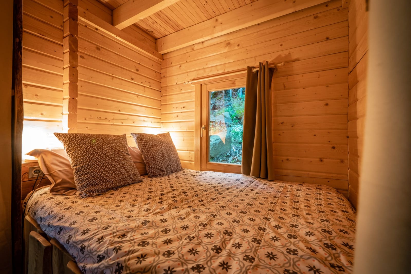 IMG-20250707-WA0018 Chalet en bois chaleureux avec lit douillet et vue sur la nature à travers la fenêtre.