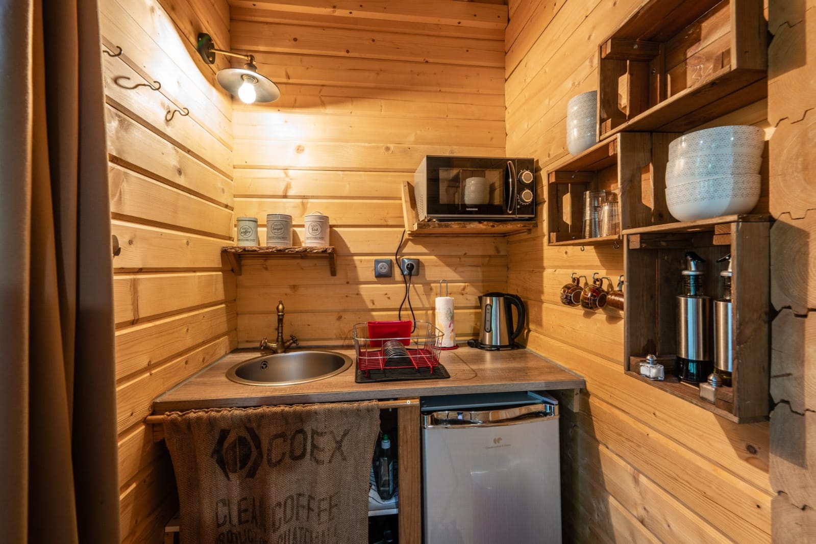 IMG-20250707-WA0019 Cuisine d'un chalet en bois, avec un évier, un réfrigérateur et des étagères décoratives.