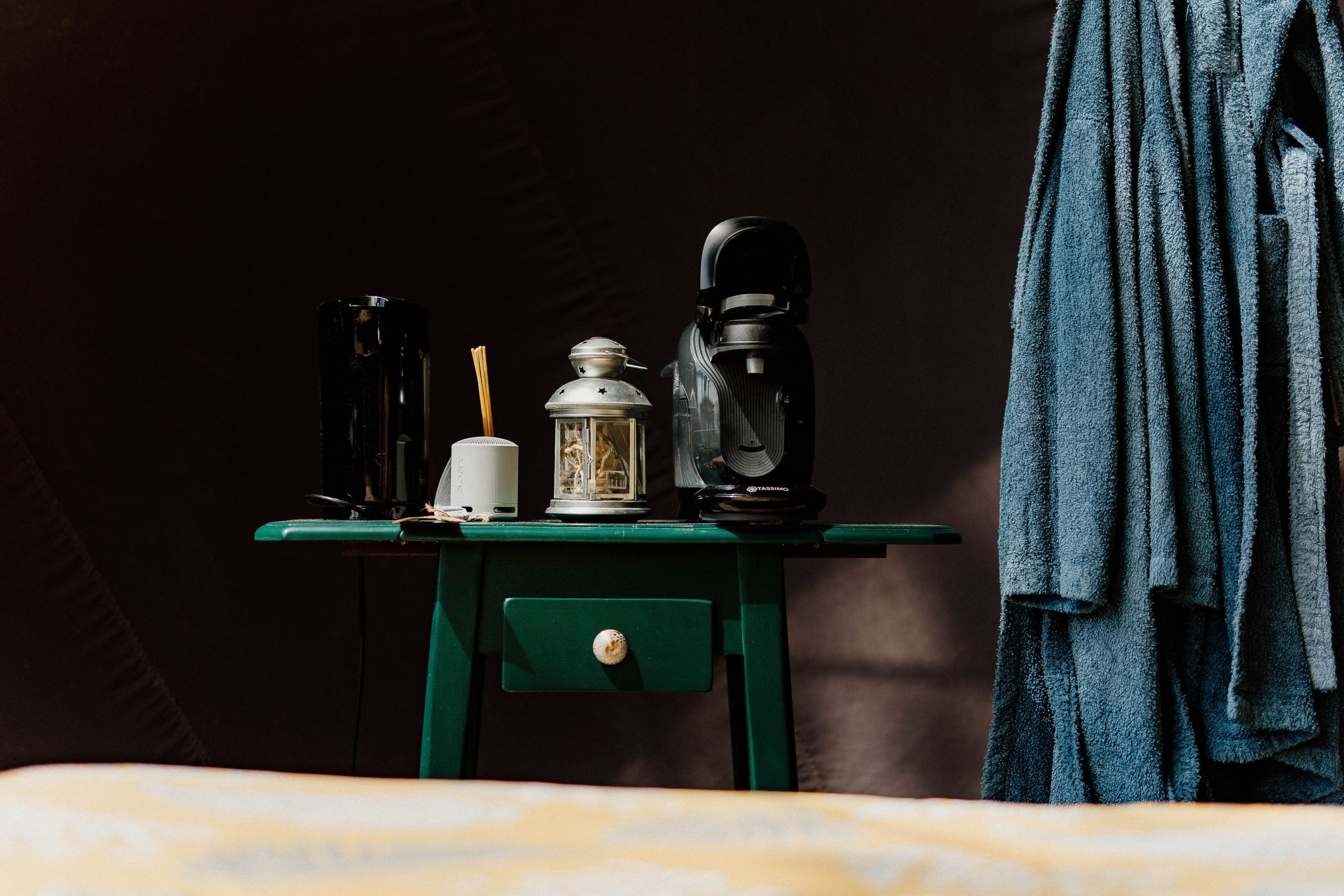 Un hébergement insolite : une table verte avec une cafetière et des peignoirs suspendus.