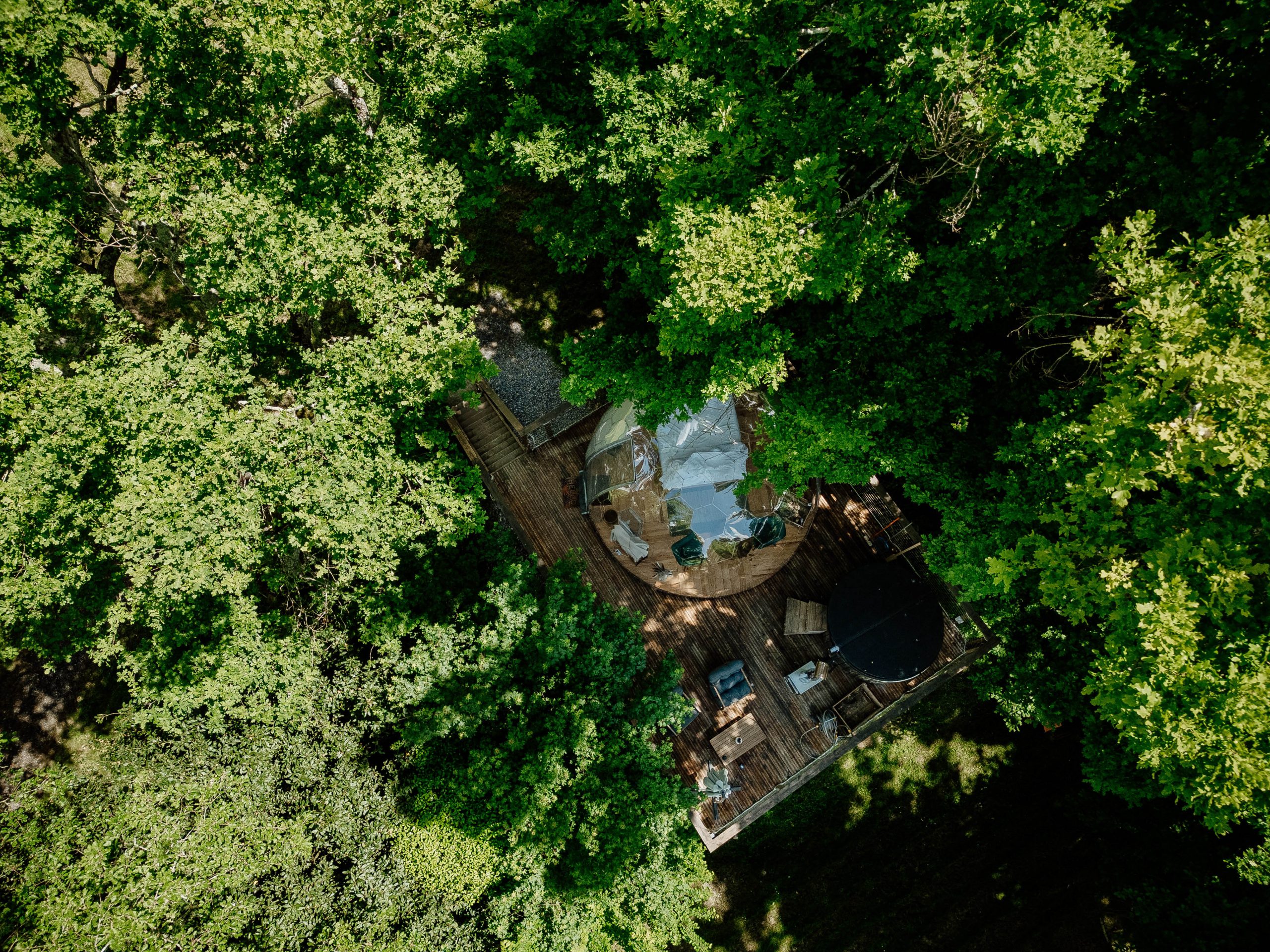 Nuit insolite_bulle_dôme_perché_occitanie_gers_Lartigue_weekend_étoiles_bain_nordique (130) Cabane perchée dans les arbres, entourée de verdure, avec terrasse en bois et spa.