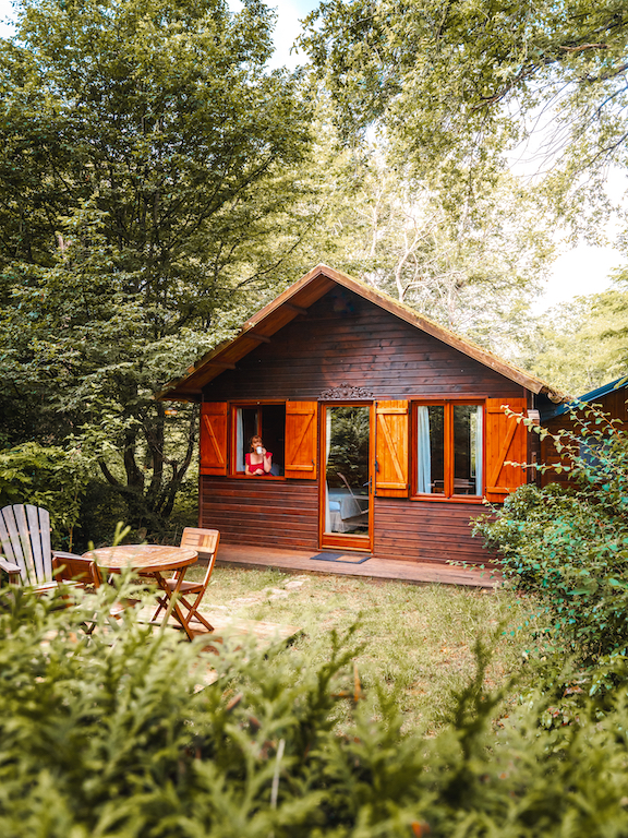PASSAGESECRET_25 Charmant chalet en bois avec volets ouverts, entouré de verdure et d'un coin repas extérieur.