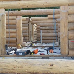 Construction d'un chalet en rondins, avec des troncs de bois apparents et des outils de chantier.