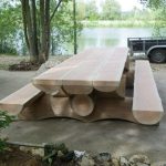 Table en bois massif au bord d'un lac, entourée d'arbres verdoyants. Ambiance paisible et naturelle.