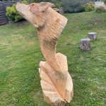 Sculpture en bois représentant un loup, dans un jardin verdoyant, hébergement insolite.