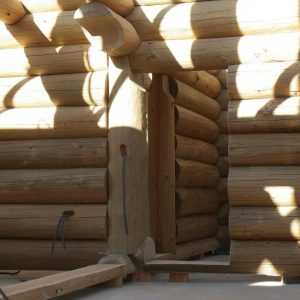 Cabane en rondins en construction, avec des murs en bois brut et des ombres graphiques.