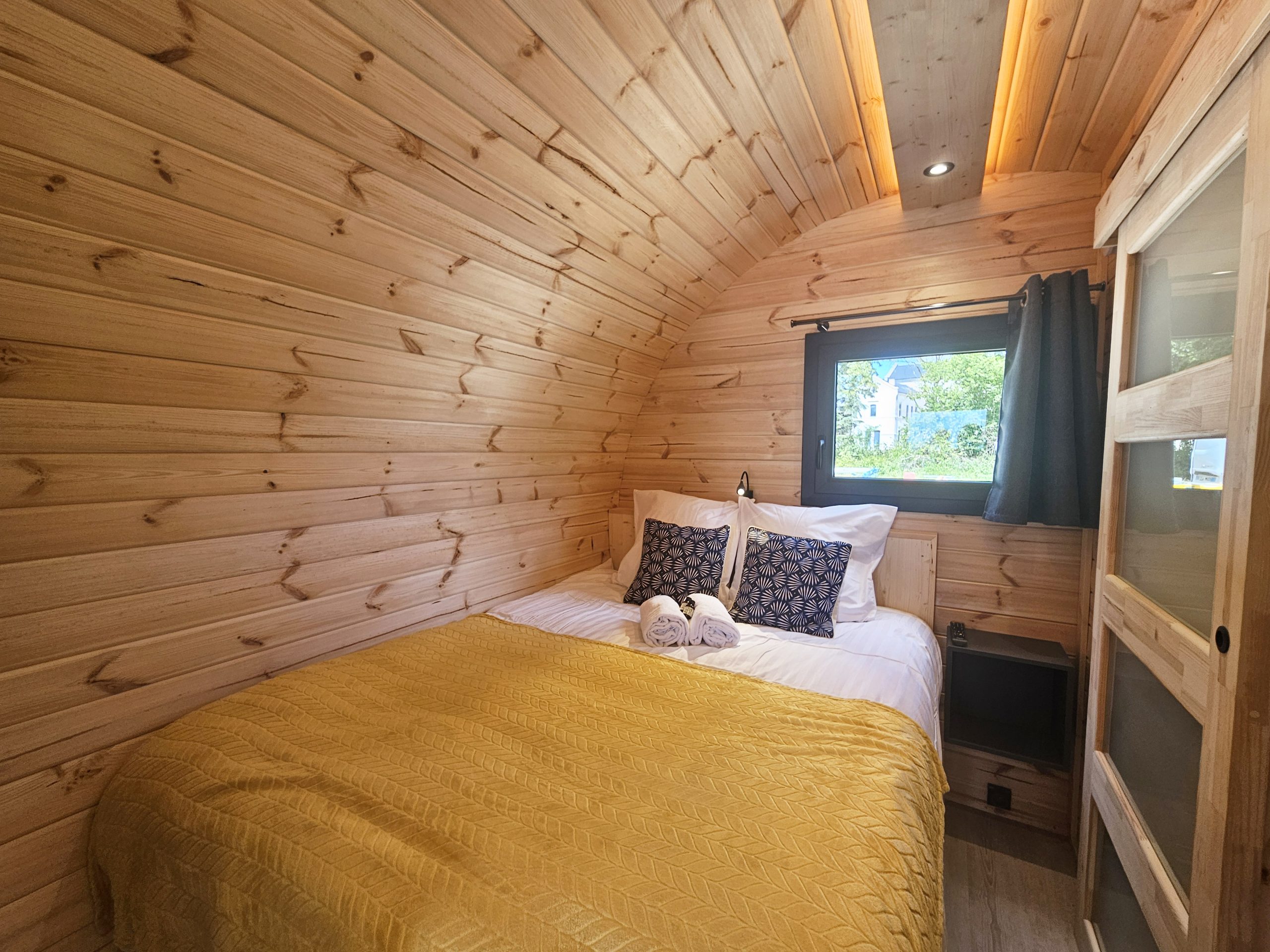 chambre Cabane en bois chaleureuse avec lit douillet, décorée de coussins élégants et d'une lumière douce.