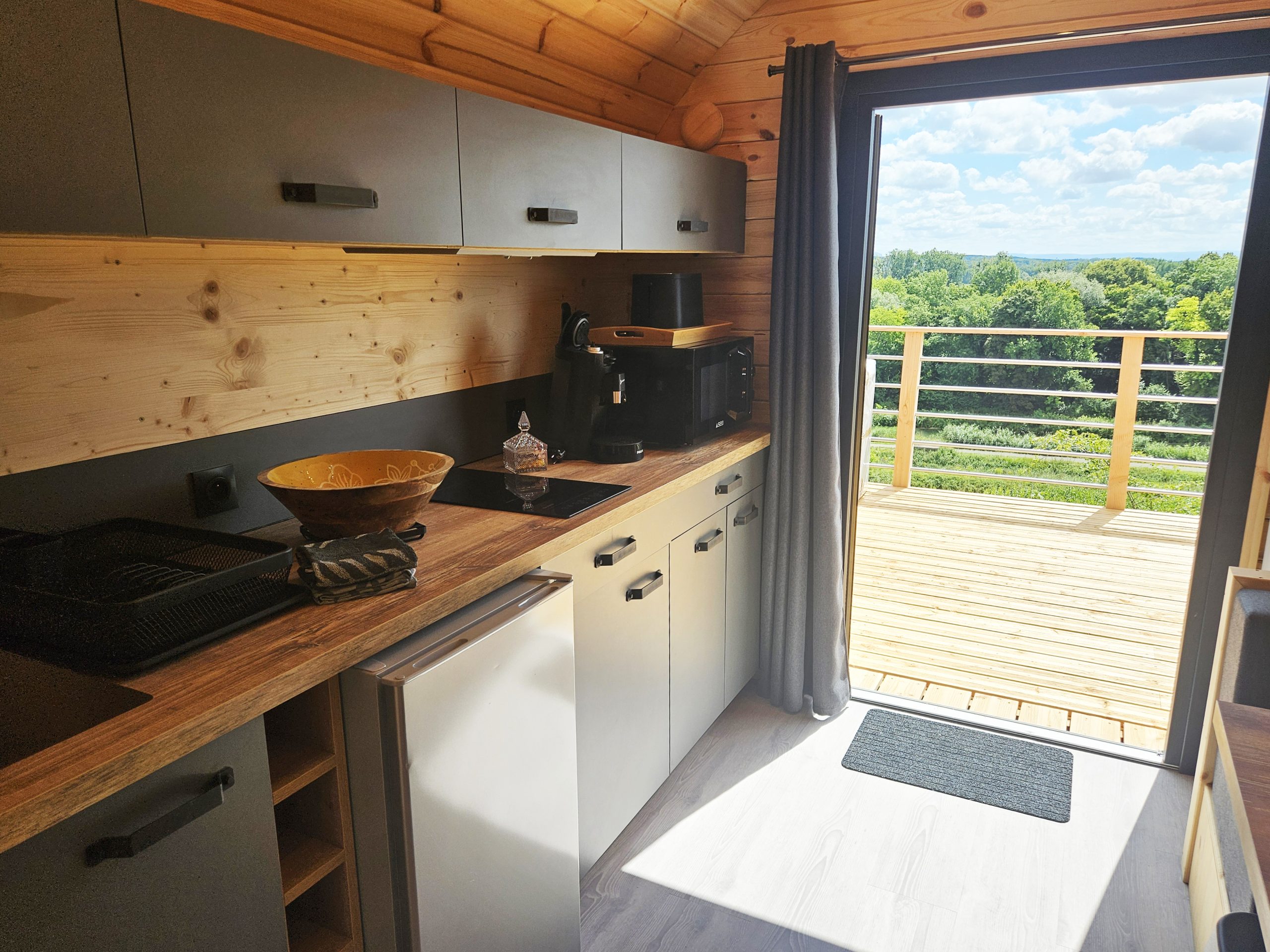 vue_cuisine_terrasse Cottage en bois avec cuisine moderne et vue dégagée sur la nature depuis la terrasse.